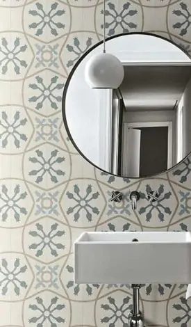 Cloakroom wall in a soft grey and blue patterned tile behind a round mirror